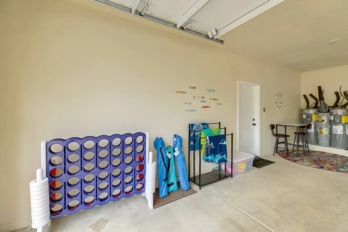 A cheerful indoor nook with a large purple Connect Four game, blue beach towels, colorful fish-themed wall décor, a small table and chairs, and pool equipment storage. The scene conveys lighthearted family fun and multi-generational enjoyment.