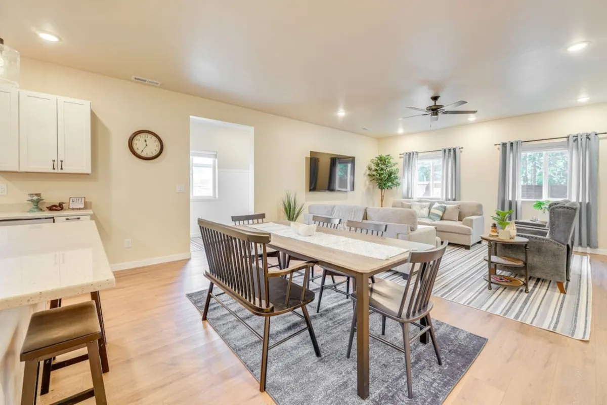A bright, open-concept living and dining area, featuring a comfortable sofa, a modern dining table set for family meals, a large Smart TV, and lush house plants bringing a touch of nature indoors. The natural light streaming in highlights the inviting atmosphere and versatility of the space.