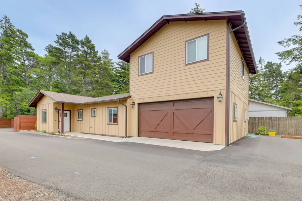 This image features the home's two-story structure with the garage door and front entrance visible, set amidst greenery. The exterior exudes warmth and approachability, with a porch area ideal for relaxing or welcoming guests after a day spent in town.