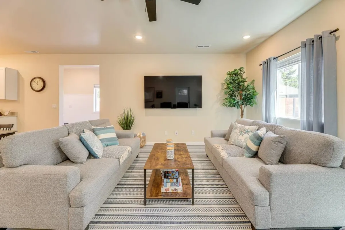 A cozy living room setup with two soft gray sofas, a wooden coffee table, decorative cushions, a large flat-screen TV, and a green plant adding vibrancy. The space is arranged for socializing, games, or movie nights, capturing a warm, communal feel.