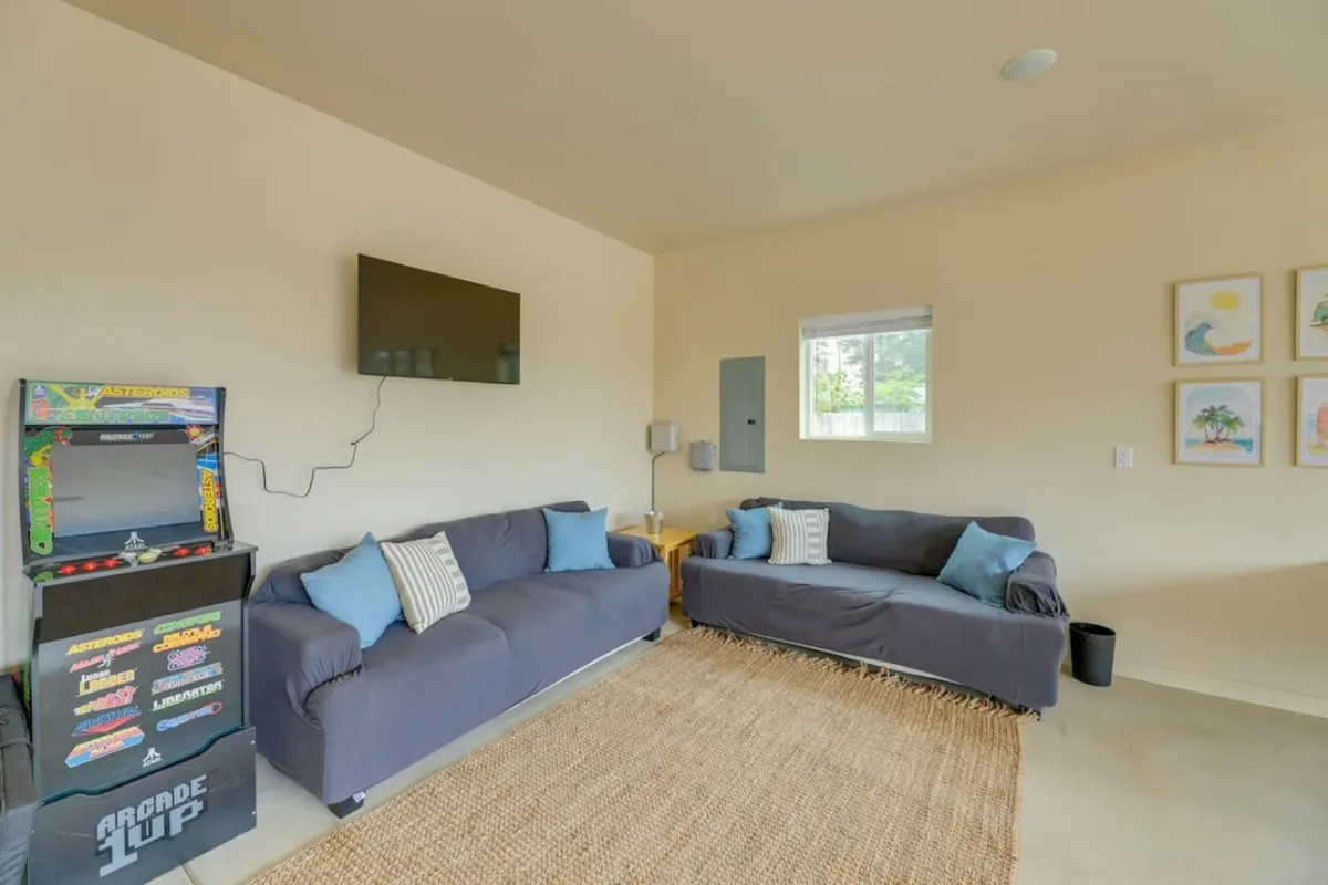 A cozy game lounge with two plush sofas arranged around an arcade game machine and a large television. The walls are decorated with vibrant artwork, creating an inviting environment for group games, movie nights, and relaxed socializing.