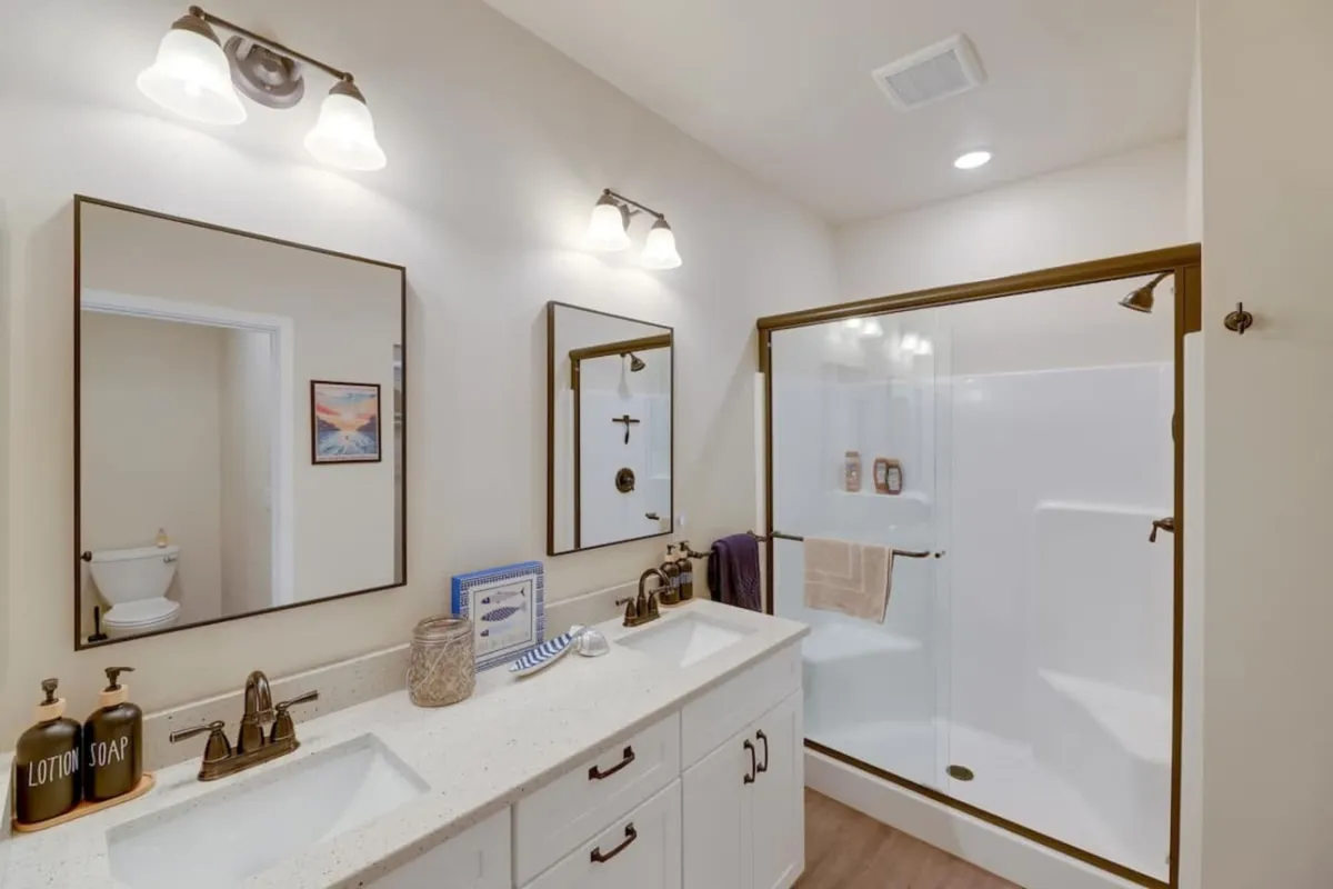 A modern bathroom featuring a double sink vanity with framed mirrors, a glass shower enclosure, and decorative soap dispensers. The space is well-lit and inviting, providing both function and relaxation for guests.